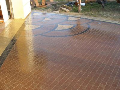 Ułożona kostka brukowa w odcieniach brązu z dekoracyjnym wzorem geometrycznym w kształcie półkola, przylegająca do ściany budynku.